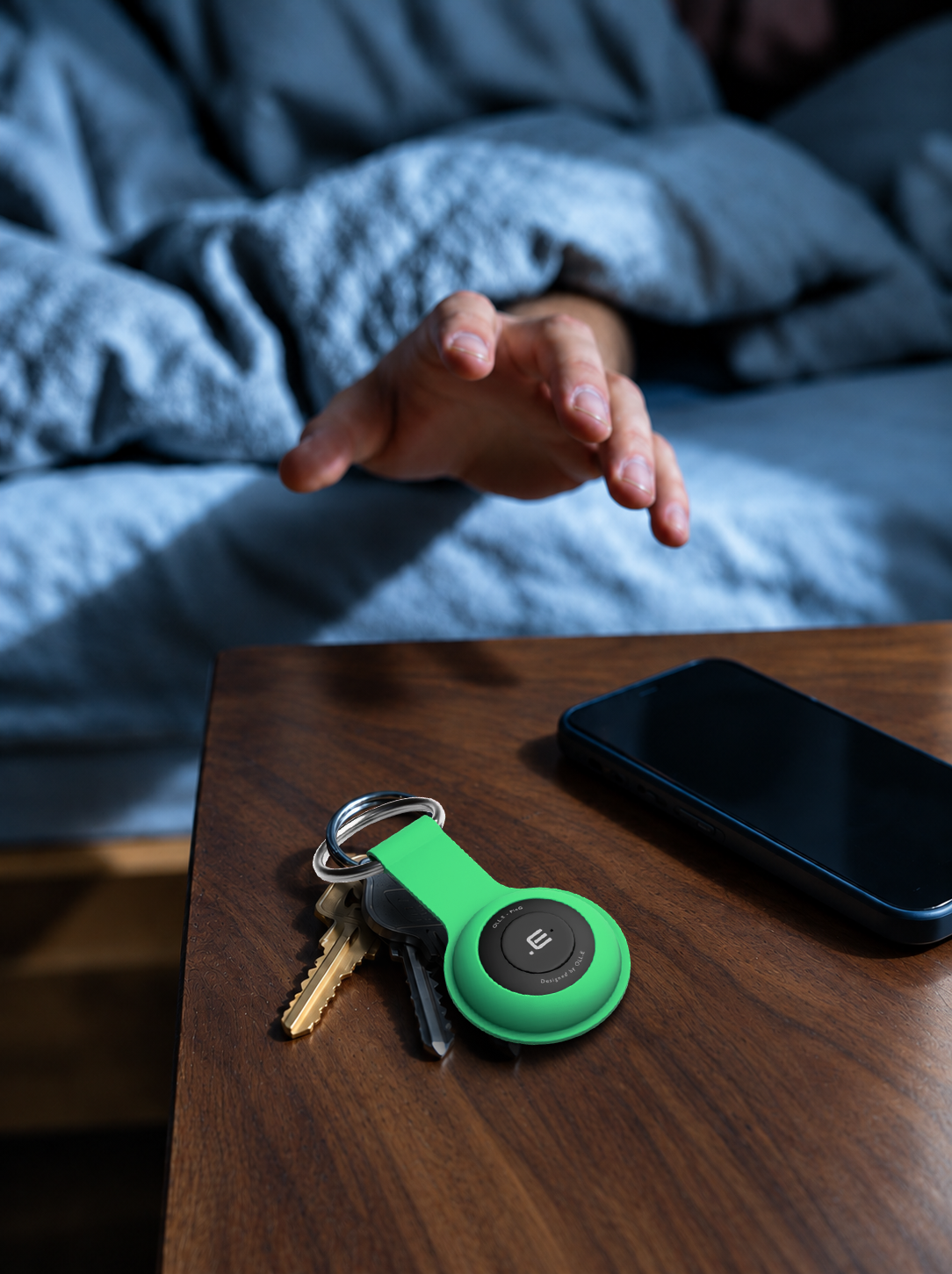 Loud enough to wake you — an Orange PinG on keys on a bedside table beside a phone, a hand reaching out from the bed